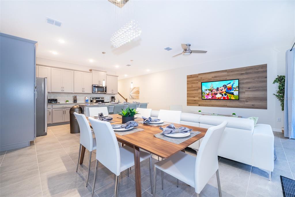 A dining area with a wooden table and white chairs sits before an open kitchen — 2166 FLEMING MIST PLACE, KISSIMMEE, FL
