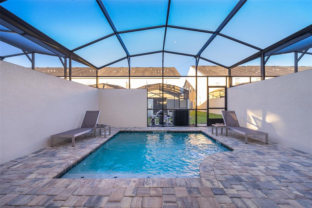 A screened-in patio features a small rectangular swimming pool surrounded by stone pavers and loungers — 2166 FLEMING MIST PLACE, KISSIMMEE, FL
