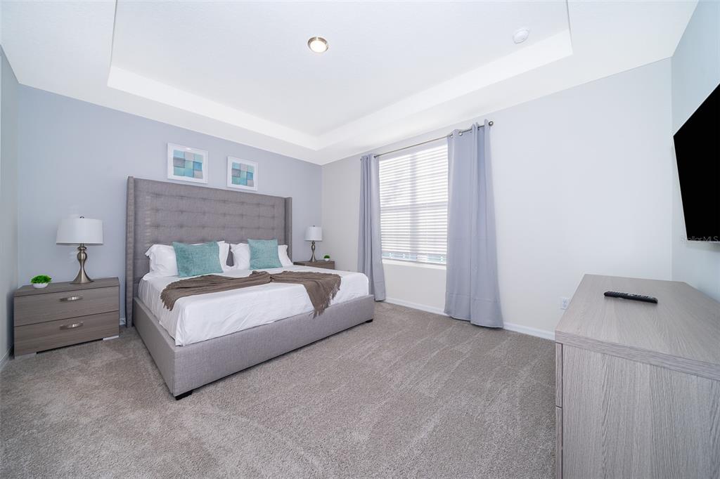 A bedroom features a gray upholstered bed, matching nightstands, and a dresser on carpeted flooring — 2166 FLEMING MIST PLACE, KISSIMMEE, FL