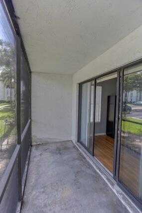 A screened-in concrete balcony features sliding glass doors leading into an interior room with wood floors — 1010 Green Pine Boulevard # E1, West Palm Beach FL 33409, WEST PALM BEACH, FL