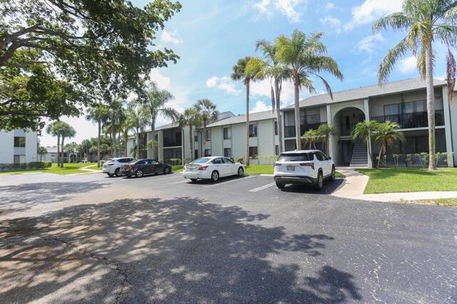 A parking lot sits in front of two-story apartment buildings surrounded by palm trees — 1010 Green Pine Boulevard # E1, West Palm Beach FL 33409, WEST PALM BEACH, FL