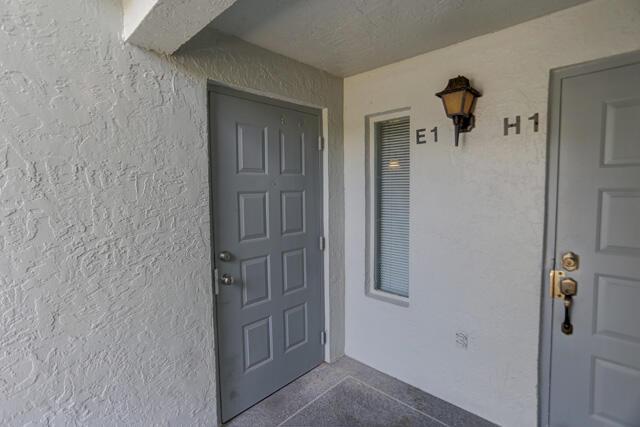 An exterior view of two gray apartment doors with a wall-mounted light fixture between them — 1010 Green Pine Boulevard # E1, West Palm Beach FL 33409, WEST PALM BEACH, FL
