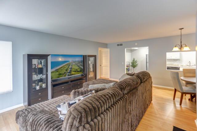 A living room with a brown textured sofa, a large television, and light wood flooring — 1010 Green Pine Boulevard # E1, West Palm Beach FL 33409, WEST PALM BEACH, FL