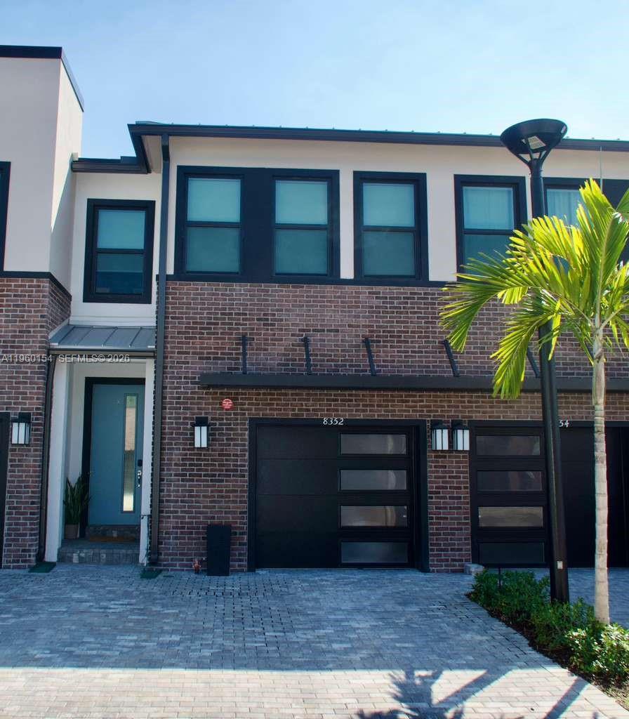 A two-story brick townhouse features a blue front door and a modern garage door — 8352 NW 7th Pl, Plantation FL 33324, PLANTATION, FL