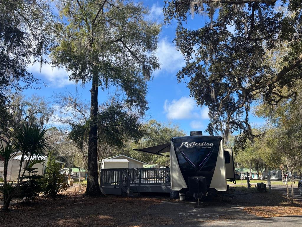 A Grand Design Reflection fifth-wheel RV is parked next to a wooden deck under trees — 25163 NE 140TH LOOP NE UNIT 17, FORT MC COY, FL