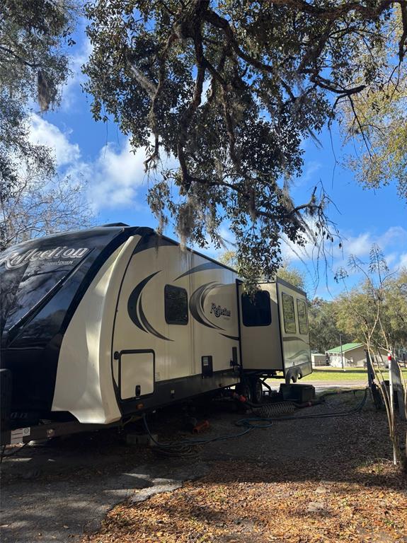 A Grand Design Reflection travel trailer is parked under large oak trees on a gravel lot — 25163 NE 140TH LOOP NE UNIT 17, FORT MC COY, FL