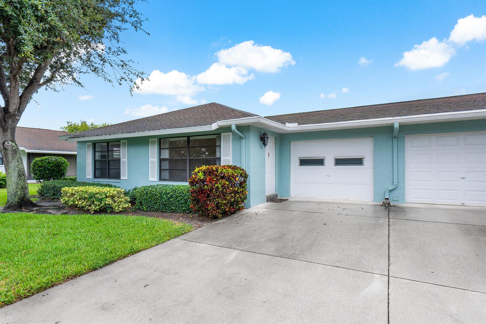 A light blue single-story house features a concrete driveway, two garage doors, and landscaping — 4360 Eucalyptus Tree Court # A, Boynton Beach FL 33436, BOYNTON BEACH, FL