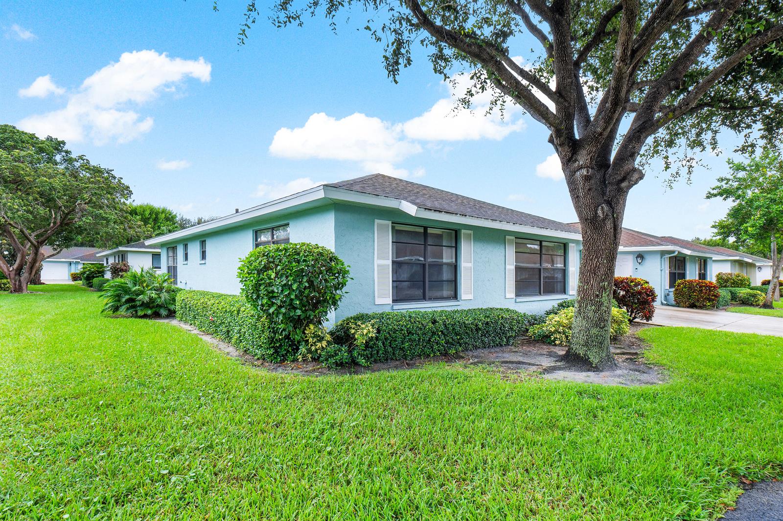 A light blue single-story house with white shutters sits on a lawn with large trees — 4360 Eucalyptus Tree Court # A, Boynton Beach FL 33436, BOYNTON BEACH, FL