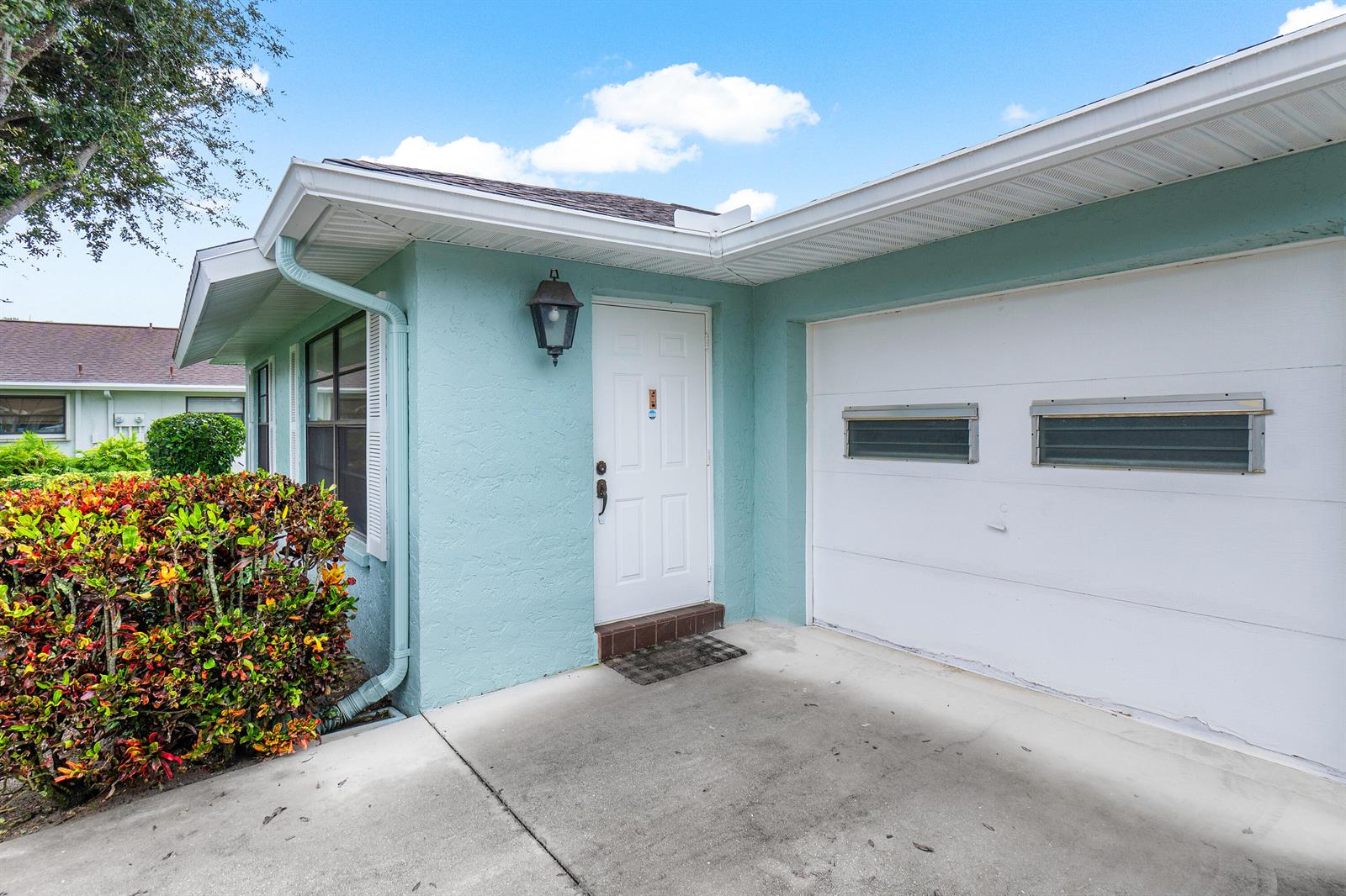 A light blue house exterior features a white front door, a garage, and a landscaped bush — 4360 Eucalyptus Tree Court # A, Boynton Beach FL 33436, BOYNTON BEACH, FL