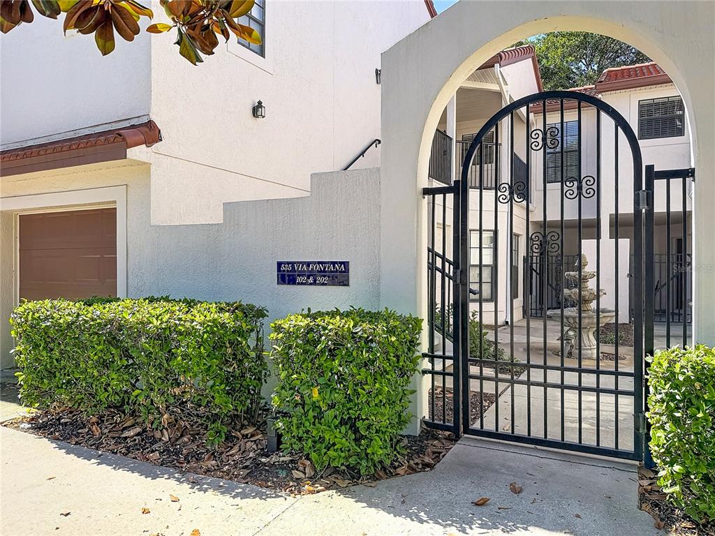 A wrought iron gate leads to a courtyard with a fountain and building entrance — 535 VIA FONTANA DRIVE UNIT 202, ALTAMONTE SPRINGS, FL