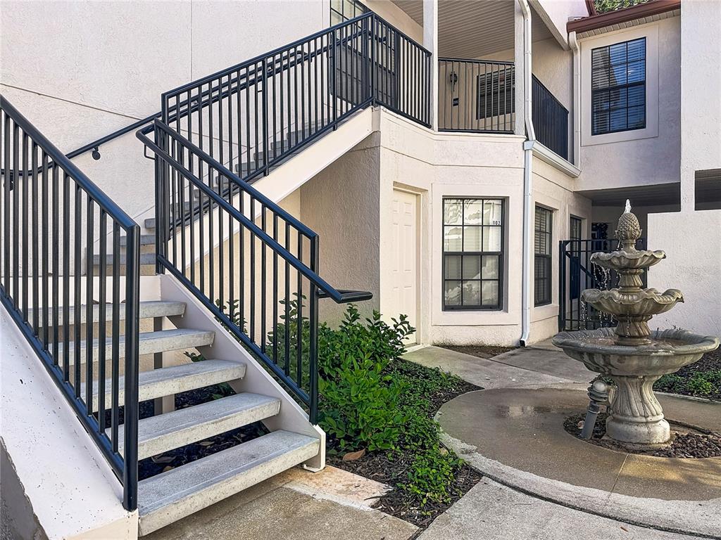 An outdoor staircase with black metal railings leads to an upper level near a fountain — 535 VIA FONTANA DRIVE UNIT 202, ALTAMONTE SPRINGS, FL