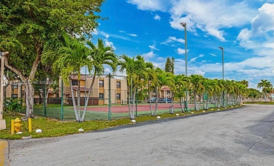 A fenced tennis court sits in front of a multi-story apartment building with palm trees — MIAMI, FL