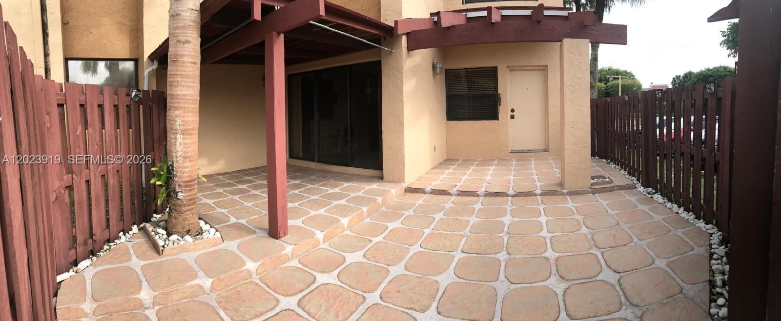 A paved patio features a palm tree, a wooden pergola, and a fenced backyard area — MIAMI, FL