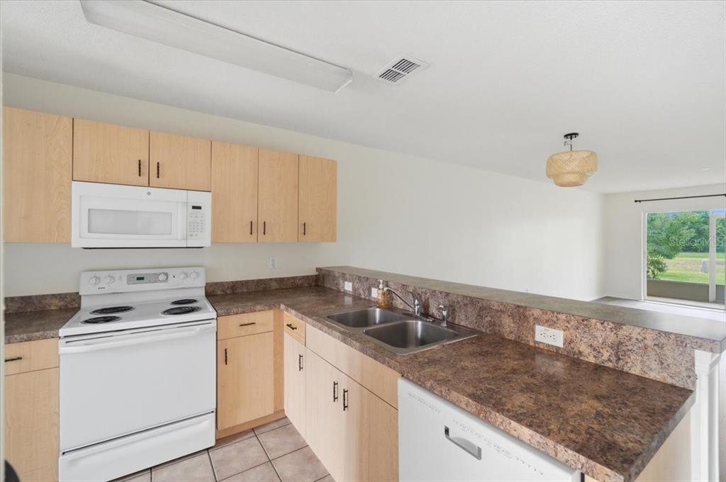 A kitchen features light wood cabinets, brown laminate countertops, white appliances, and a tile floor — 212 OCEAN BLUFF DRIVE, POINCIANA, FL