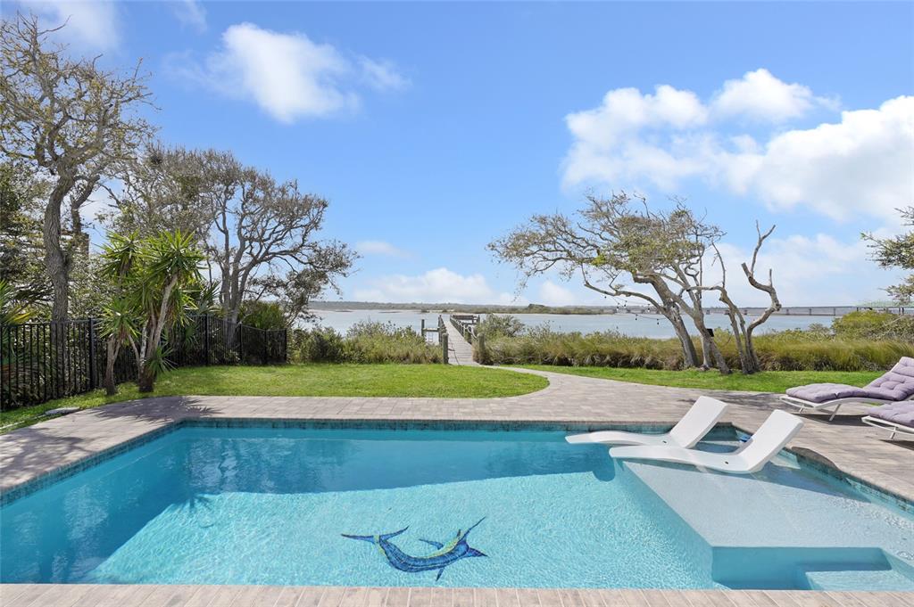 A swimming pool with a marlin mosaic overlooks a grassy yard, trees, and a wooden dock — 7101 MIDDLETON AVENUE, ST AUGUSTINE, FL