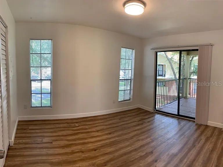 An empty room features wood-look flooring, two windows, and a sliding glass door to a balcony — 8625 MALLARD RESERVE DRIVE UNIT 204, TAMPA, FL