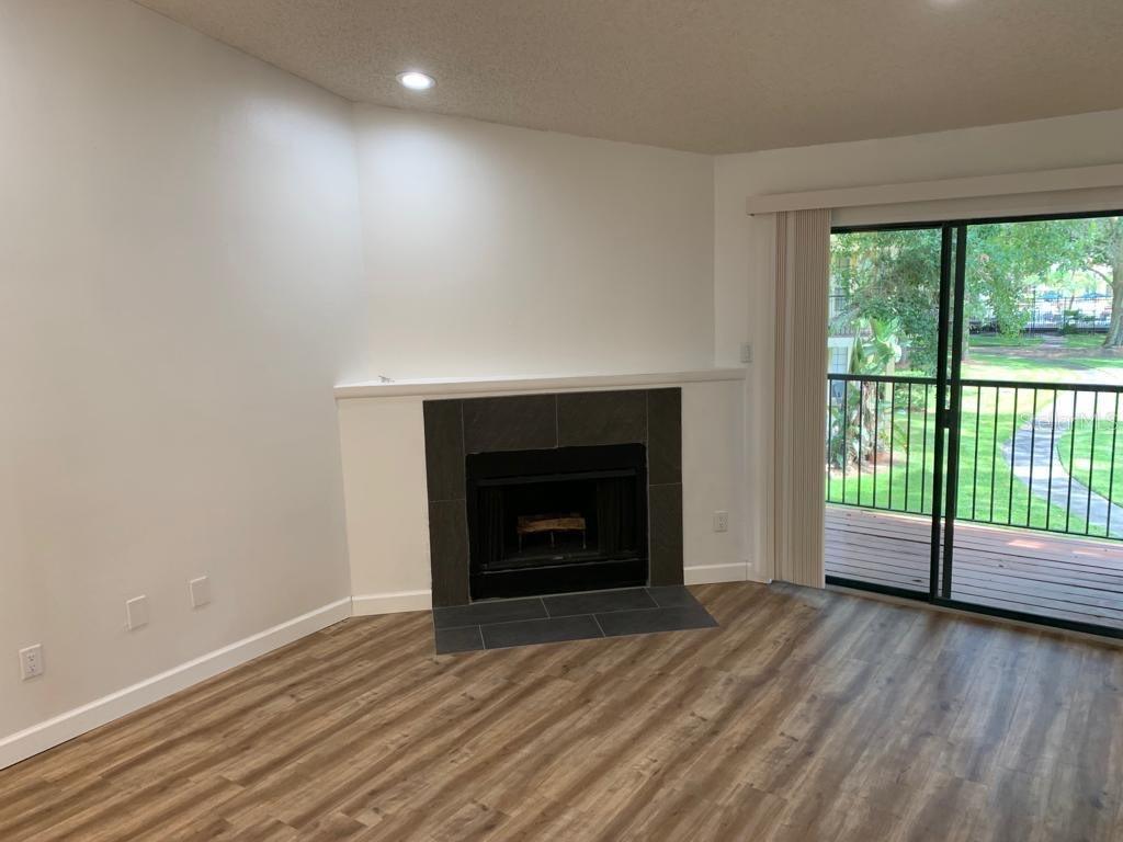 A living room with wood-look flooring, a dark tile fireplace, and a sliding glass door — 8625 MALLARD RESERVE DRIVE UNIT 204, TAMPA, FL