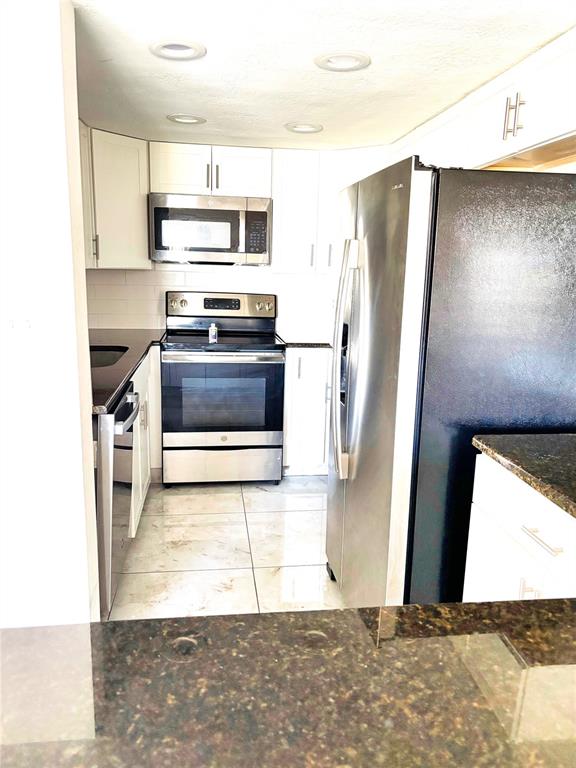A kitchen features stainless steel appliances, white cabinetry, and dark granite countertops — 2583 COUNTRYSIDE BOULEVARD UNIT 3309, CLEARWATER, FL