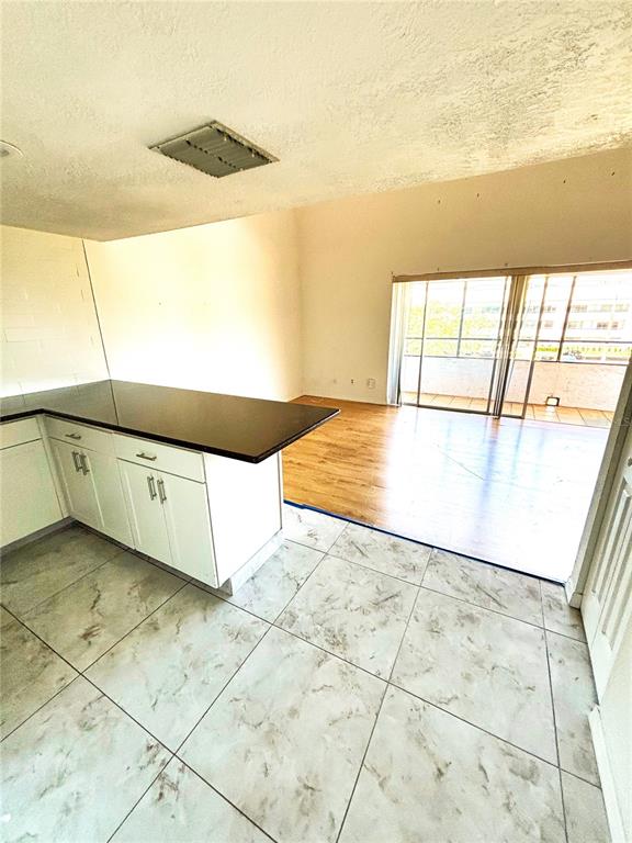 A kitchen with white cabinets and a dark countertop overlooks a living area with flooring — 2583 COUNTRYSIDE BOULEVARD UNIT 3309, CLEARWATER, FL