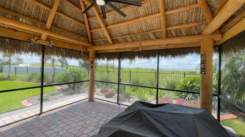 A screened-in patio with a thatched roof, ceiling fan, and paver floor overlooks a grassy yard — 3015 WOOD DUCK DRIVE, POLK CITY, FL