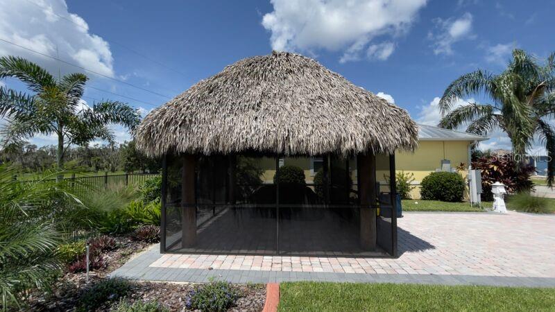 A thatched-roof tiki hut sits on a paved patio next to a yellow house — 3015 WOOD DUCK DRIVE, POLK CITY, FL