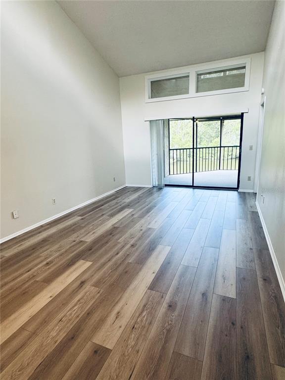 A living room with vaulted ceilings, wood-look flooring, and a sliding glass door to a balcony — 328 WOODLAKE WYNDE, OLDSMAR, FL