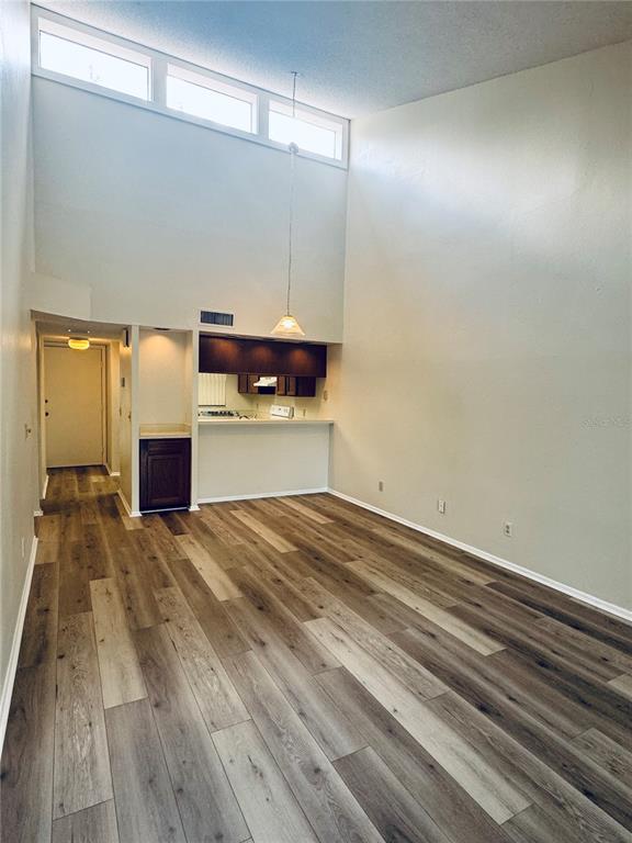 A living room with high ceilings, large windows, and wood-look flooring leads to a kitchen — 328 WOODLAKE WYNDE, OLDSMAR, FL