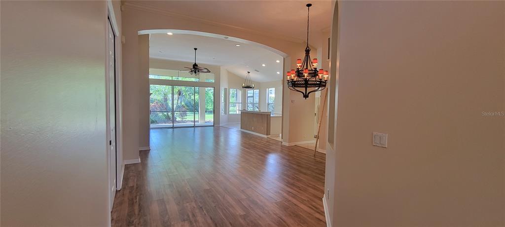 An open-concept living area features wood-look flooring, a large chandelier, and sliding glass doors — 7217 ORCHID ISLAND PLACE, BRADENTON, FL