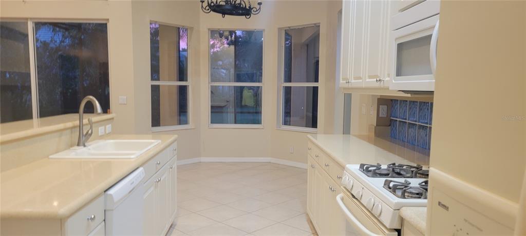 A kitchen with white cabinets, light countertops, a gas stove, and a breakfast nook area — 7217 ORCHID ISLAND PLACE, BRADENTON, FL