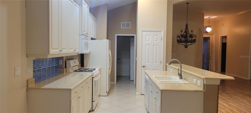 A kitchen with white cabinets, beige countertops, and a breakfast bar overlooking an adjacent room — 7217 ORCHID ISLAND PLACE, BRADENTON, FL
