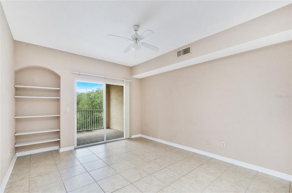 An empty room with beige tile floors, a built-in arched bookshelf, and a sliding glass door — 826 CAMARGO WAY UNIT 210, ALTAMONTE SPRINGS, FL