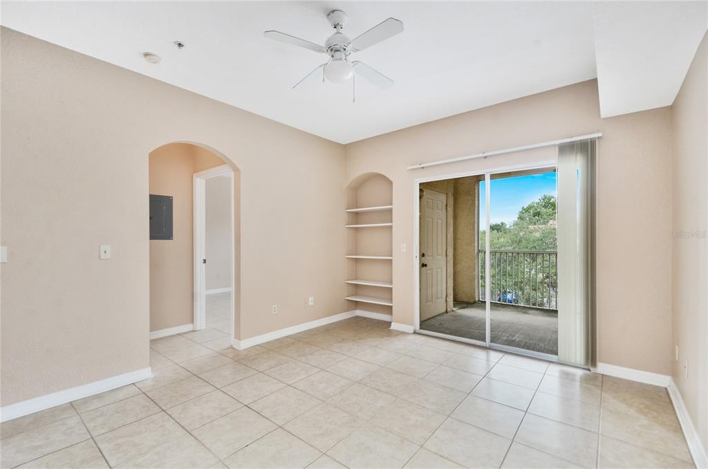 An empty room features beige tile flooring, a ceiling fan, built-in shelves, and a balcony — 826 CAMARGO WAY UNIT 210, ALTAMONTE SPRINGS, FL