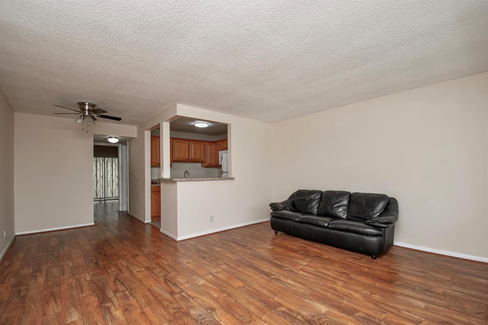 A living room with wood-look flooring, a black leather sofa, and an open kitchen pass-through — 197 Andover H, West Palm Beach FL 33417, WEST PALM BEACH, FL