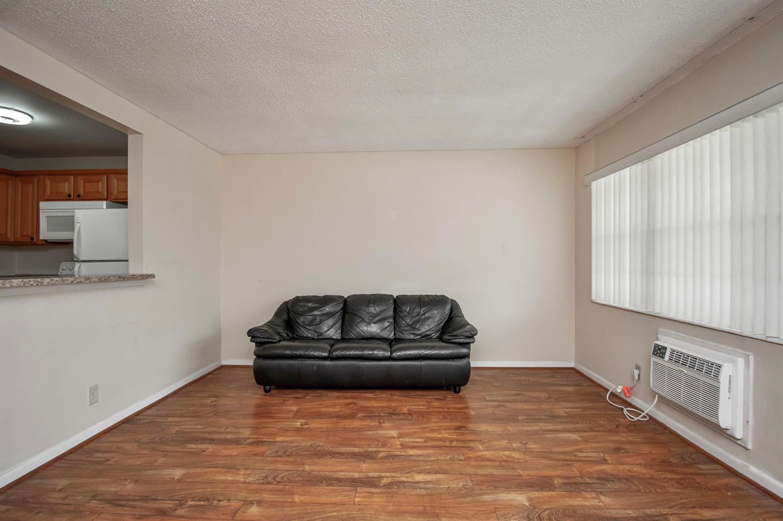 A living room features wood-look flooring, a black leather sofa, and a wall-mounted air conditioner — 197 Andover H, West Palm Beach FL 33417, WEST PALM BEACH, FL