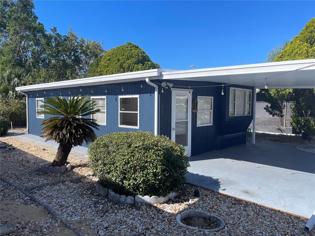A blue mobile home features a carport, a small palm tree, and a landscaped yard — 237 PALM CREST LANE, DAVENPORT, FL