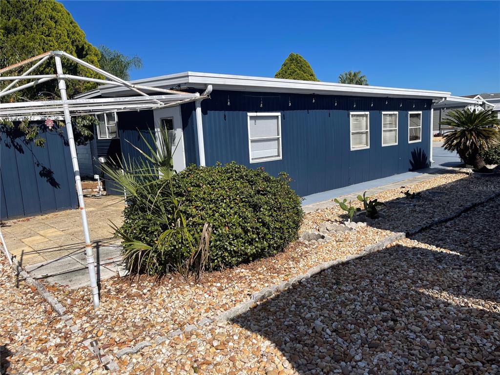 The exterior of a blue mobile home features a gravel yard and a metal awning — 237 PALM CREST LANE, DAVENPORT, FL