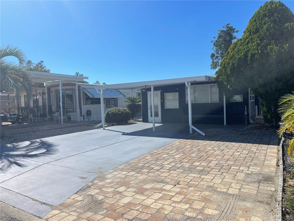 A dark-painted mobile home features a paved driveway, a carport, and a brick-paver parking area — 237 PALM CREST LANE, DAVENPORT, FL