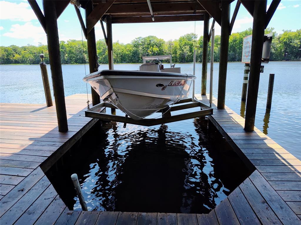 A white motorboat sits on a mechanical lift inside a wooden boat house on water — 55342 CLAIRE STREET, ASTOR, FL