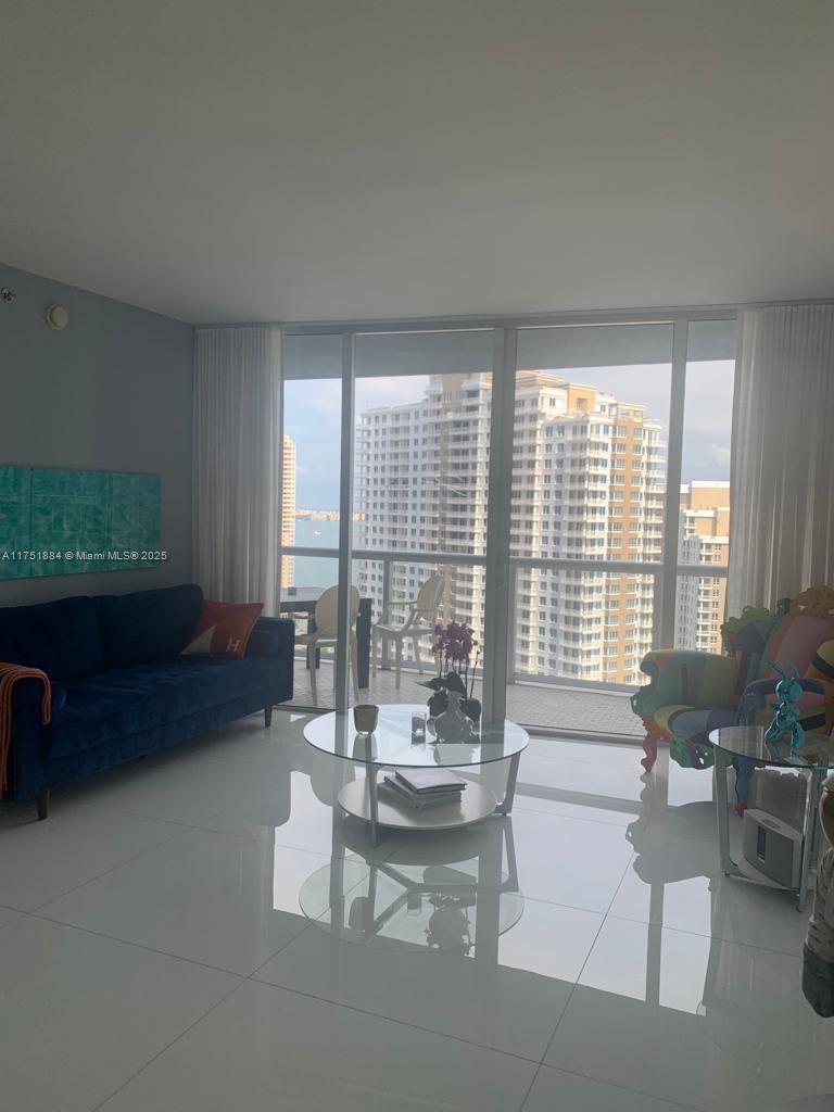 A living room features a blue sofa, colorful accent chairs, a glass coffee table, and balcony views — 465 Brickell Ave # 2405, Miami FL 33131, MIAMI, FL