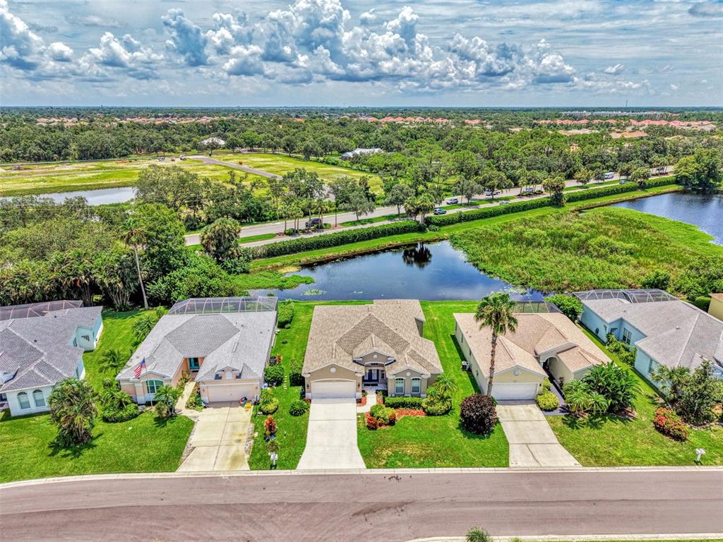An aerial view shows three suburban houses with driveways facing a street and a pond — 6339 STURBRIDGE COURT, SARASOTA, FL