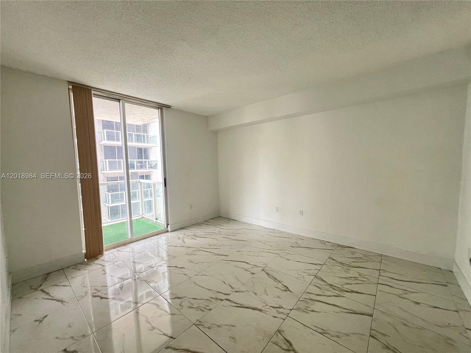 An empty room features white marble-look tile flooring, white walls, and a sliding glass door — 5085 NW 7th St # 711, Miami FL 33126, MIAMI, FL