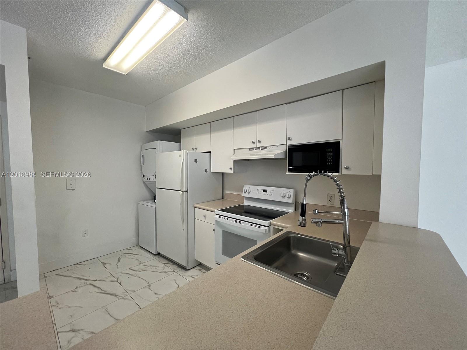 A kitchen features white cabinets, white appliances, a stainless steel sink, and marble-look tile flooring — 5085 NW 7th St # 711, Miami FL 33126, MIAMI, FL
