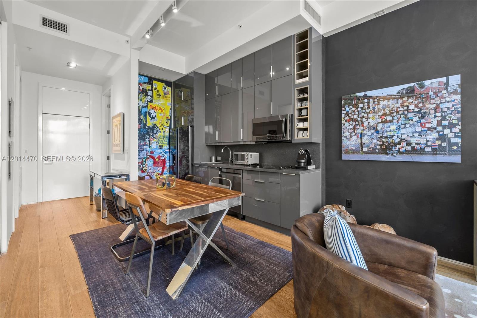 A modern kitchen features gray cabinets, a wooden dining table, and a dark accent wall — 2001 Meridian Ave # 404, Miami Beach FL 33139, MIAMI BEACH, FL