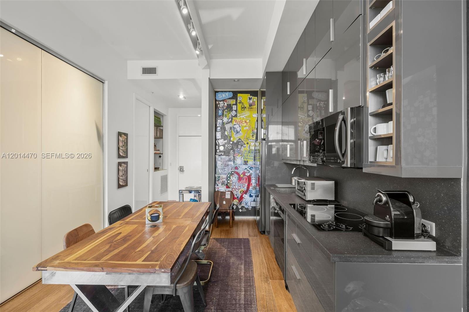A modern kitchen features dark gray cabinetry, a wooden dining table, and a sticker-covered door — 2001 Meridian Ave # 404, Miami Beach FL 33139, MIAMI BEACH, FL