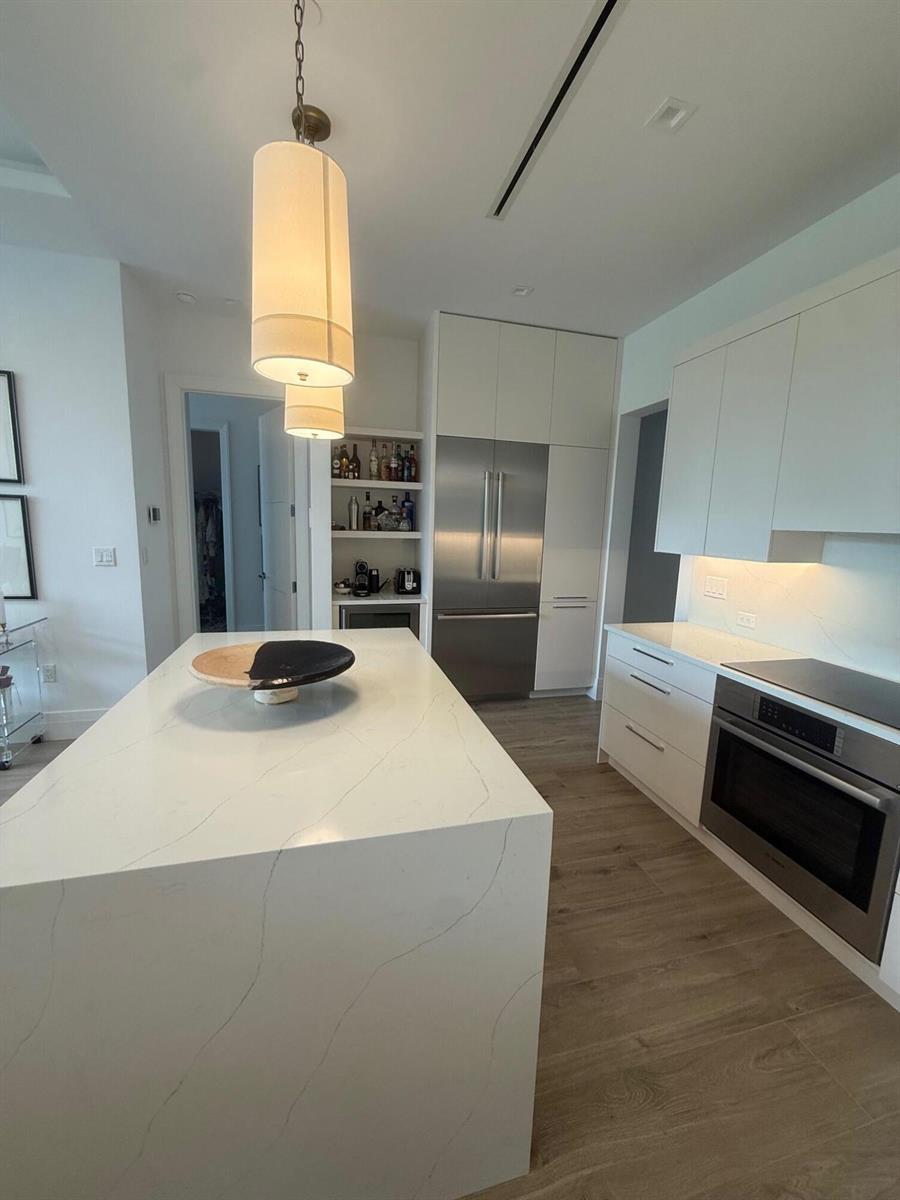 A modern kitchen features a large white quartz island, stainless steel appliances, and wood-look flooring — 1177 George Bush Boulevard # 207, Delray Beach FL 33483, DELRAY BEACH, FL