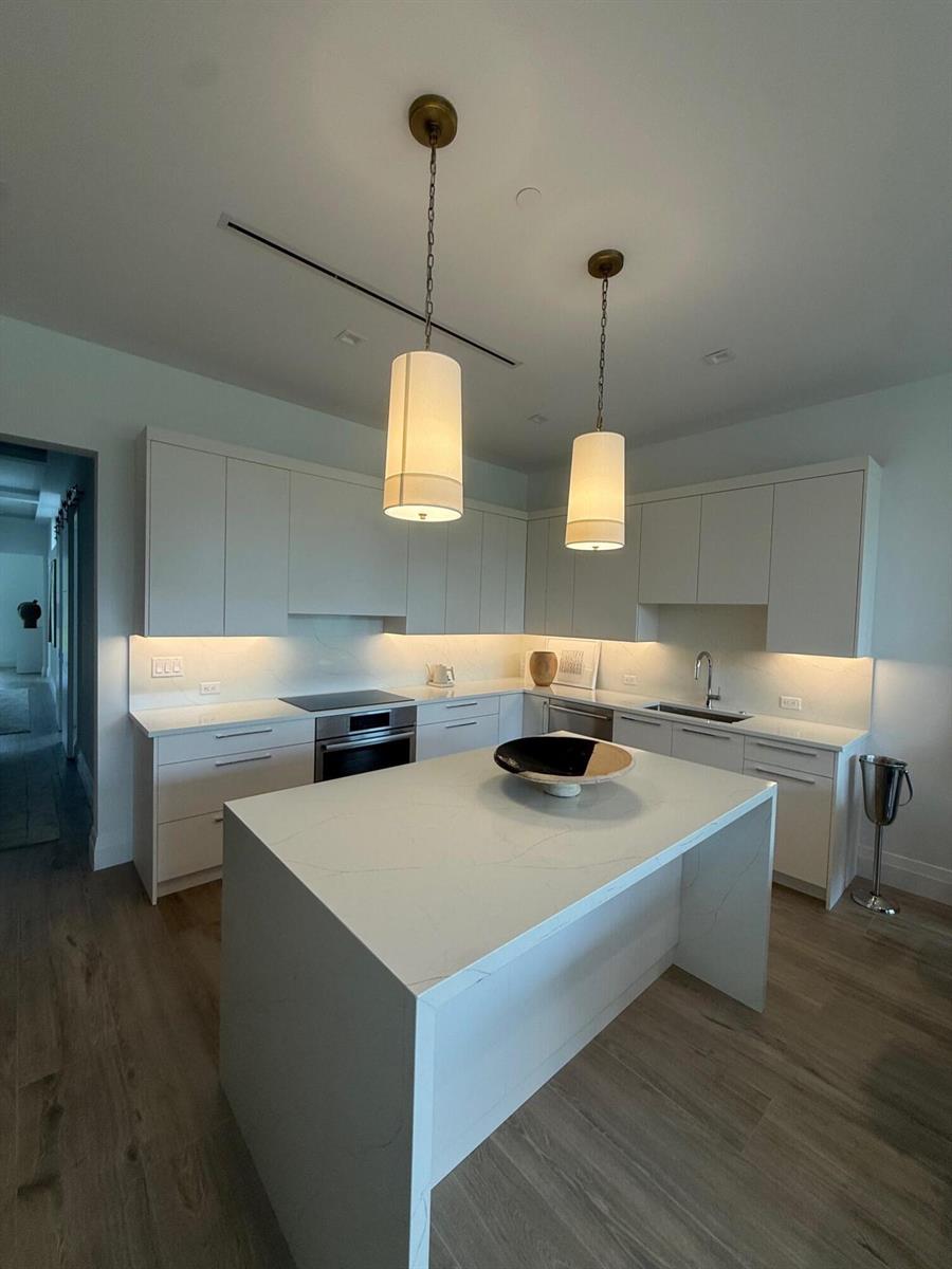 A modern kitchen features white cabinetry, a quartz island, and two pendant lights over the counter — 1177 George Bush Boulevard # 207, Delray Beach FL 33483, DELRAY BEACH, FL