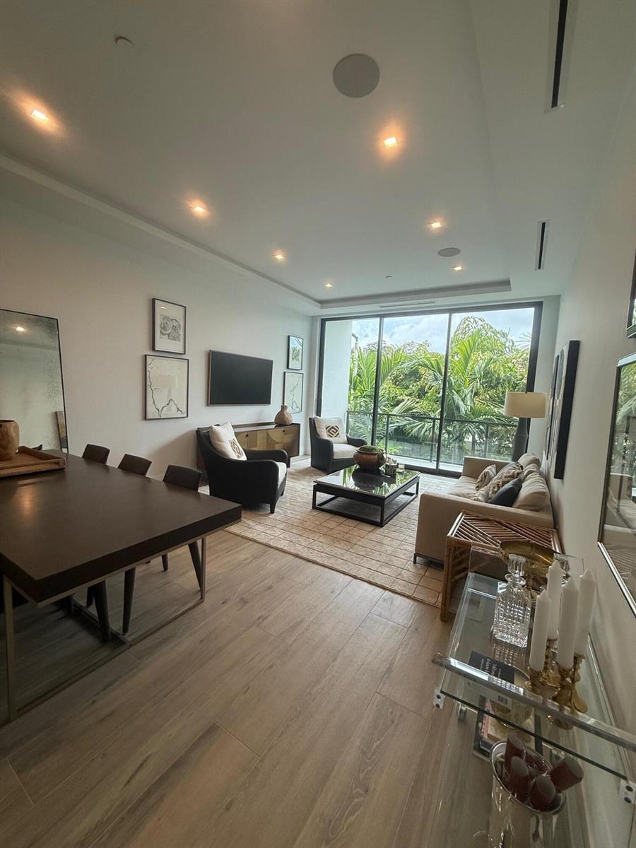 A modern living and dining room features wood-look flooring, a balcony, and neutral furnishings — 1177 George Bush Boulevard # 207, Delray Beach FL 33483, DELRAY BEACH, FL