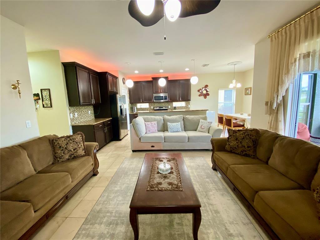An open-concept living room features two brown sofas, a central coffee table, and a kitchen — 10812 ANCIENT FUTURES DRIVE, TAMPA, FL