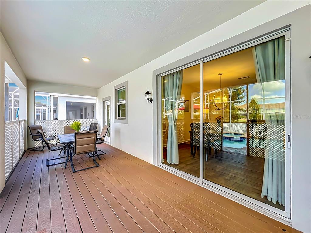 A covered wooden deck features outdoor furniture and a sliding glass door leading inside — 1556 MAIDSTONE COURT, DAVENPORT, FL