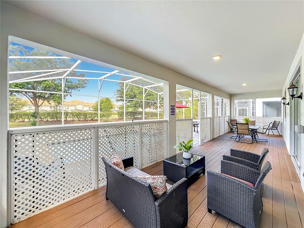 A covered patio features wicker furniture, wood-look flooring, and a screened enclosure overlooking a yard — 1556 MAIDSTONE COURT, DAVENPORT, FL